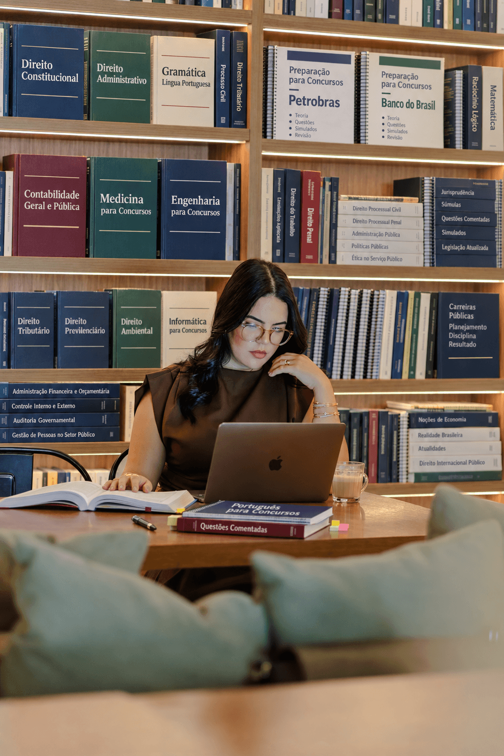 Pessoa estudando para concursos com livros, apostilas e notebook